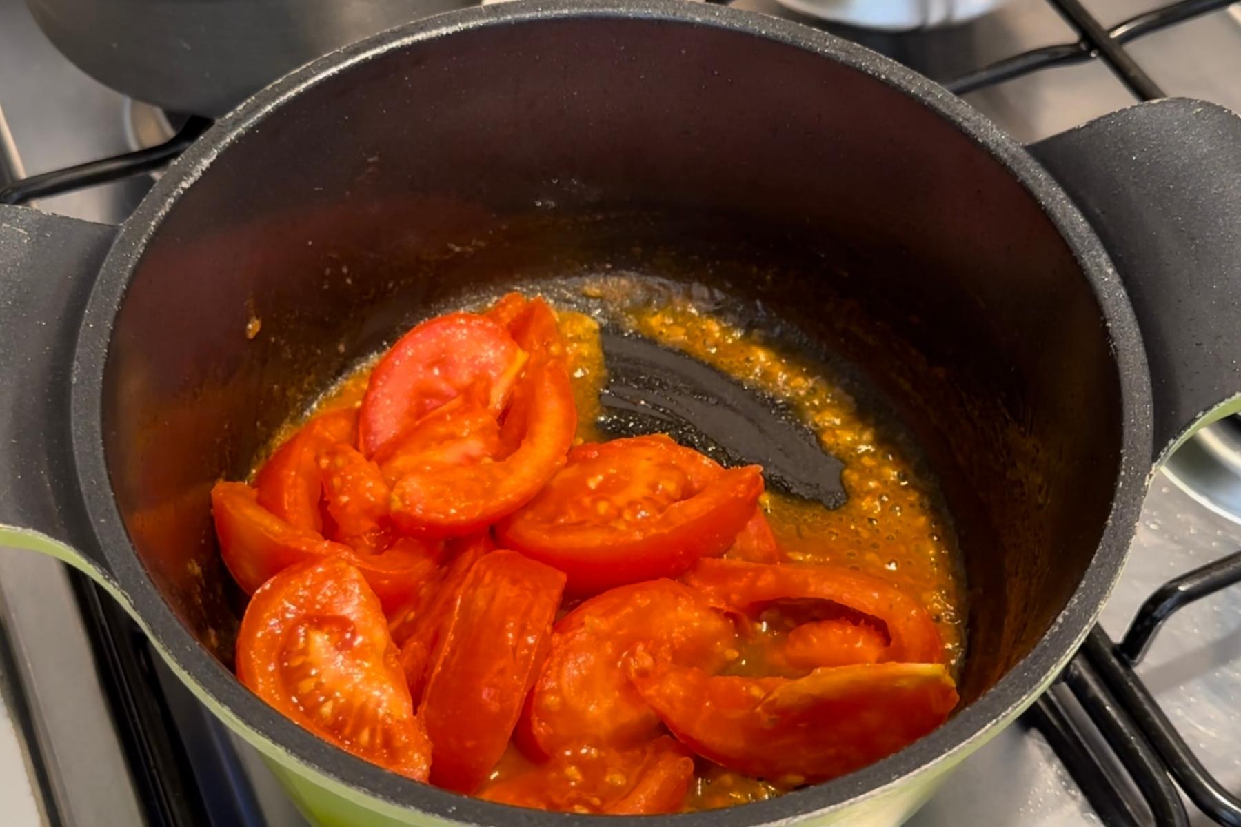 Tomato wedges simmering in a pot on a stovetop, with visible juice and seeds at the bottom.