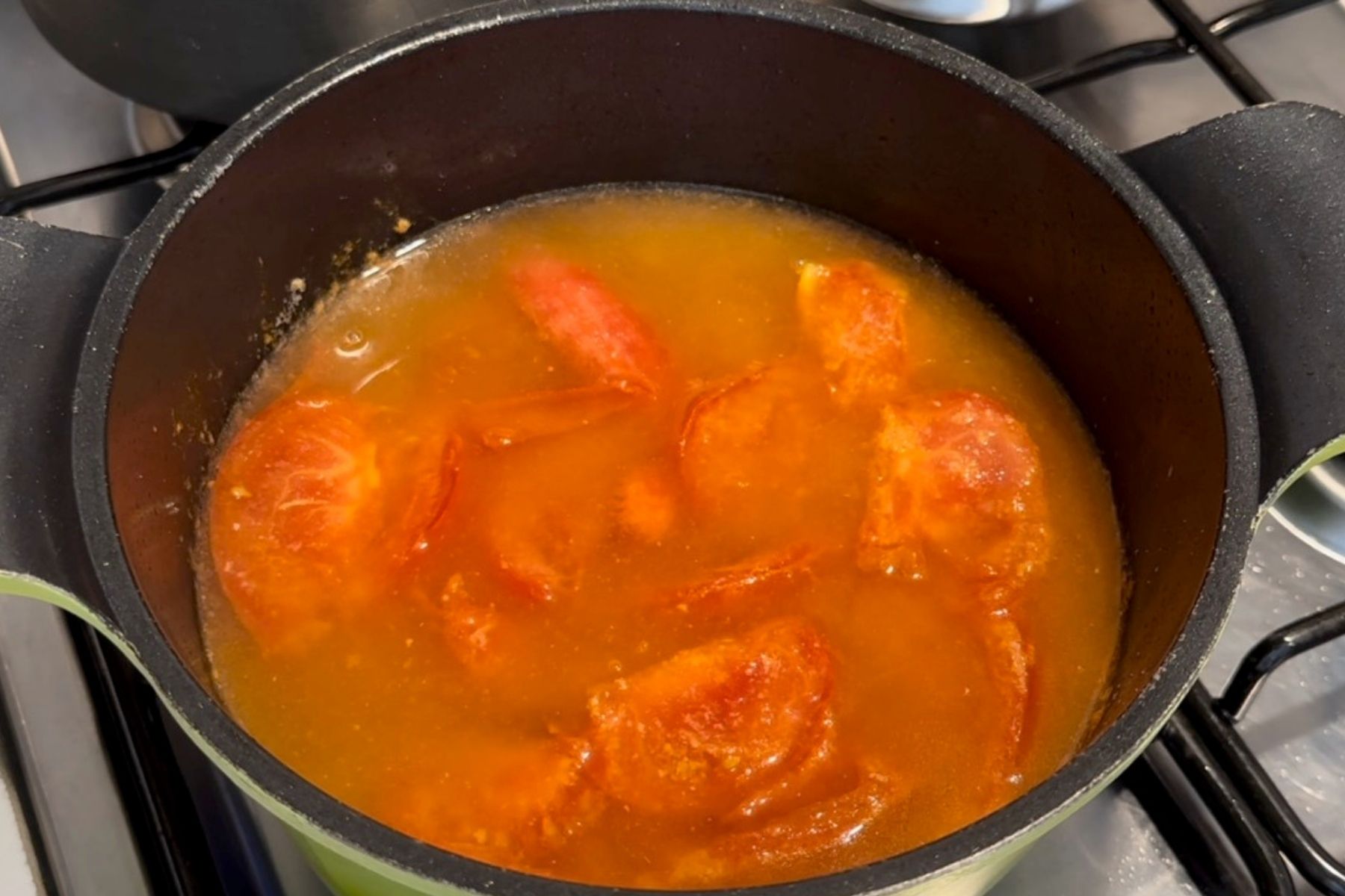 Tomato pieces simmer in broth inside a black pot on the stove.