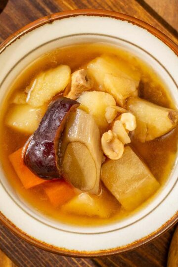 An overhead view of a bowl of burdock root soup, with a wooden spoon next to it, on wooden surfaces.