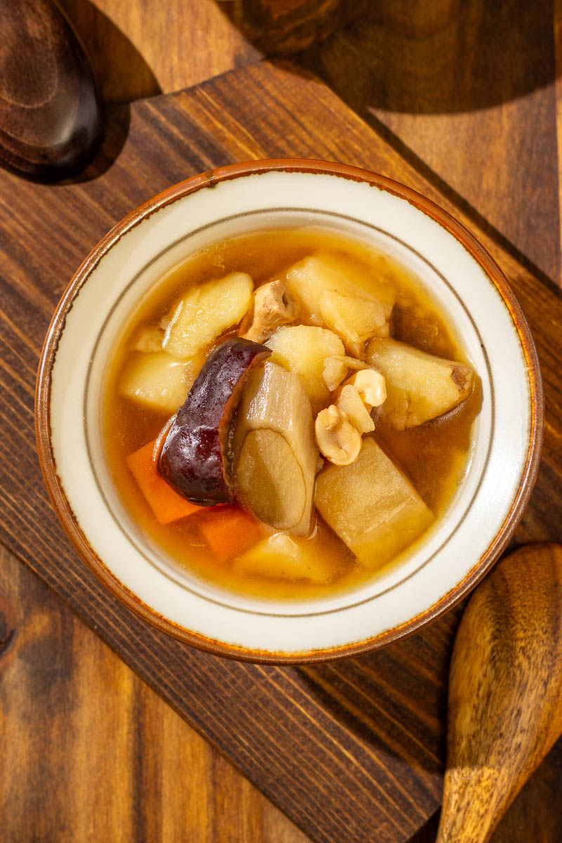 An overhead view of a bowl of burdock root soup, with a wooden spoon next to it, on wooden surfaces.