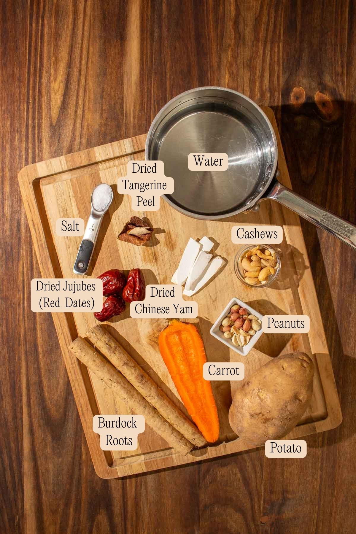 Ingredients to make burdock root soup laid out on a wooden chopping board on a wooden surface and labeled.