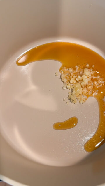 Pressed garlic being fried in sesame oil in a beige-colored pot.