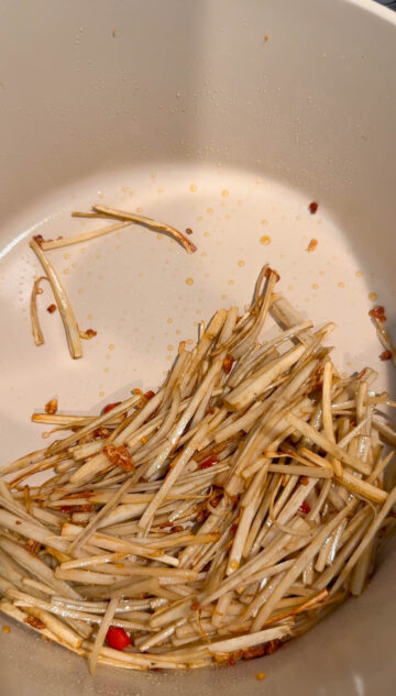 Burdock roots and Thai chili pepper, wilted and browned, in a beige-color pot.