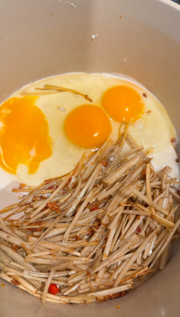 Three eggs added to the stir-fried burdock roots and Thai chili pepper in a beige-color pot.