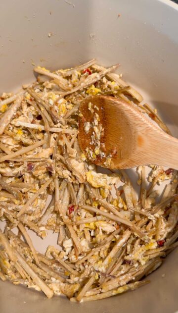 Stir-fried burdock roots and Thai chili peppers covered in egg mixture in a beige-colored pot.
