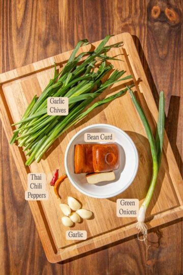 Fresh ingredients required to make Chinese Garlic Chives Bean Curd Stir Fry, laid out on a wooden chopping board and labeled.