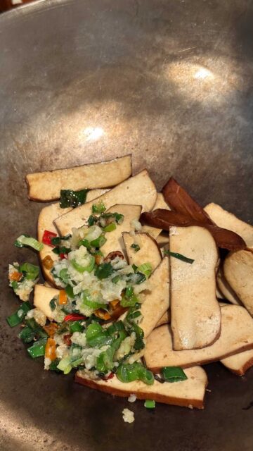 Bean curd slices, chopped green onions, garlic, and red Thai chili peppers cooking in a wok.