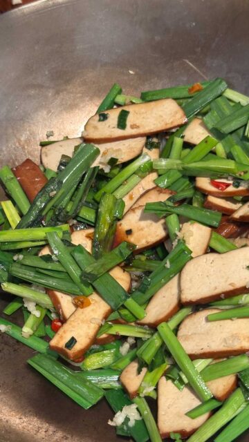 Bean curd slices and chopped Chinese garlic chives cooking in a wok.