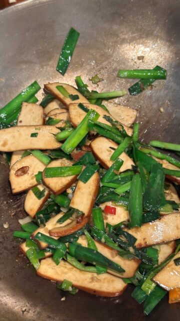 Cooked bean curd slices and chopped Chinese garlic chives in a wok.