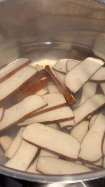 Bean curd slices being blanched in a pot of water.