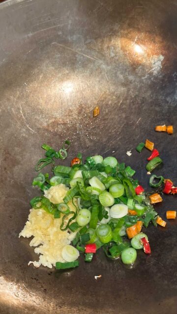 Chopped green onions, garlic, and red Thai chili peppers cooking in a wok.