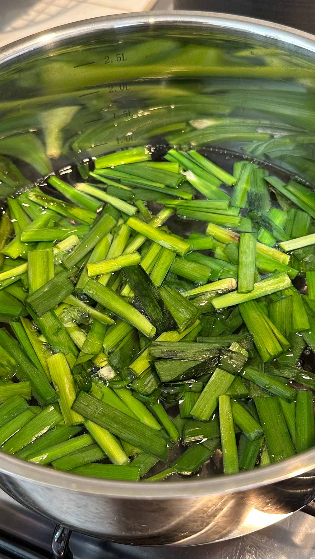 Chopped garlic chives blanching in pot of water on a stove.