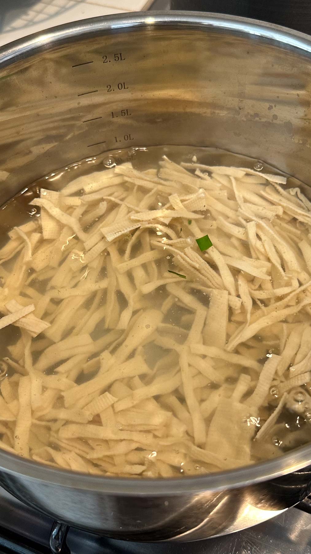 Dried tofu noodles blanching in pot of water on a stove.