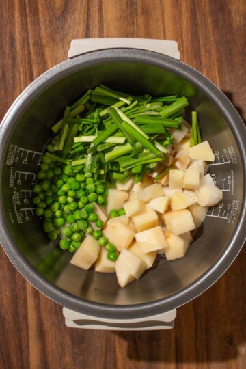 Chinese garlic chives, chunks of potato and bamboo shoots, and green peas in a rice cooker pot on a wooden surface—an easy rice cooker meal.