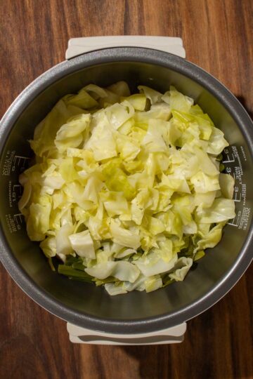 A bed of chopped and cooked cabbage in a rice cooker pot on a wooden surface.
