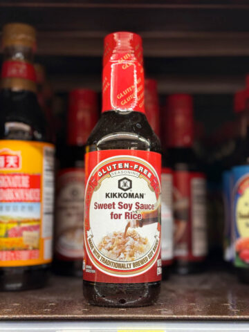 A bottle of Kikkoman Gluten-Free Sweet Soy Sauce for Rice sits on a store shelf, with others in the background.