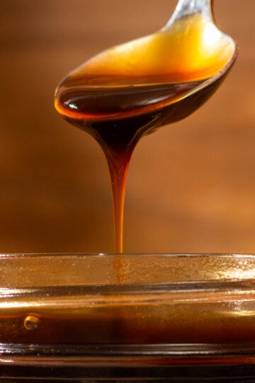 A spoon drizzles thick soy sauce into a glass jar against a warm brown background. // AtypicalFare.com.