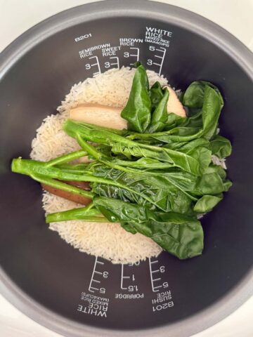 Cooked white rice, gai lan, king oyster mushrooms, and vegan sausage in a rice cooker pot.