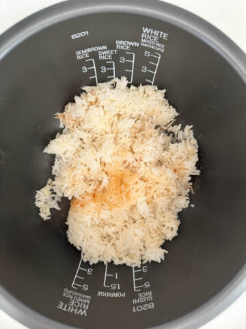 Cooked white rice with some browning at the bottom, inside a rice cooker pot with measurement markings.