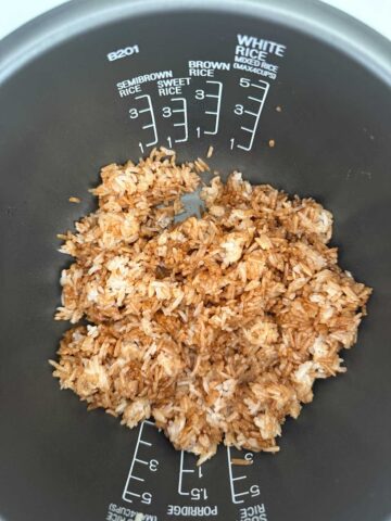 Cooked white rice mixed with sweet soy sauce in a rice cooker pot.