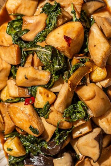 A three cup chicken-inspired vegetarian dish of stir-fried king oyster mushroom, basils, and three cup sauce served in an oval plate on a wooden surface.