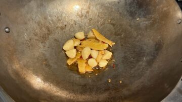 Garlic and ginger slices sautéing in sesame oil in a wok.