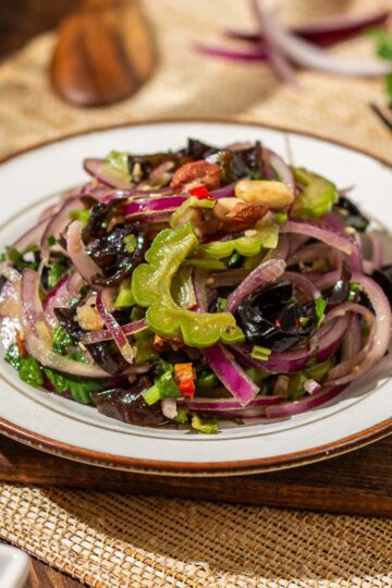 A plate of Chinese Bitter Melon Salad with bitter melon, woodear mushrooms, red onions, peanuts, sesame seeds, and Thai chili peppers, served on a rustic table.
