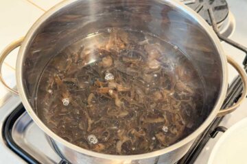 Sliced woodear mushrooms being blanched in a pot of water on a stove.