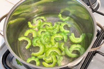 Sliced bitter melon boiling in a stainless steel pot on a stovetop.