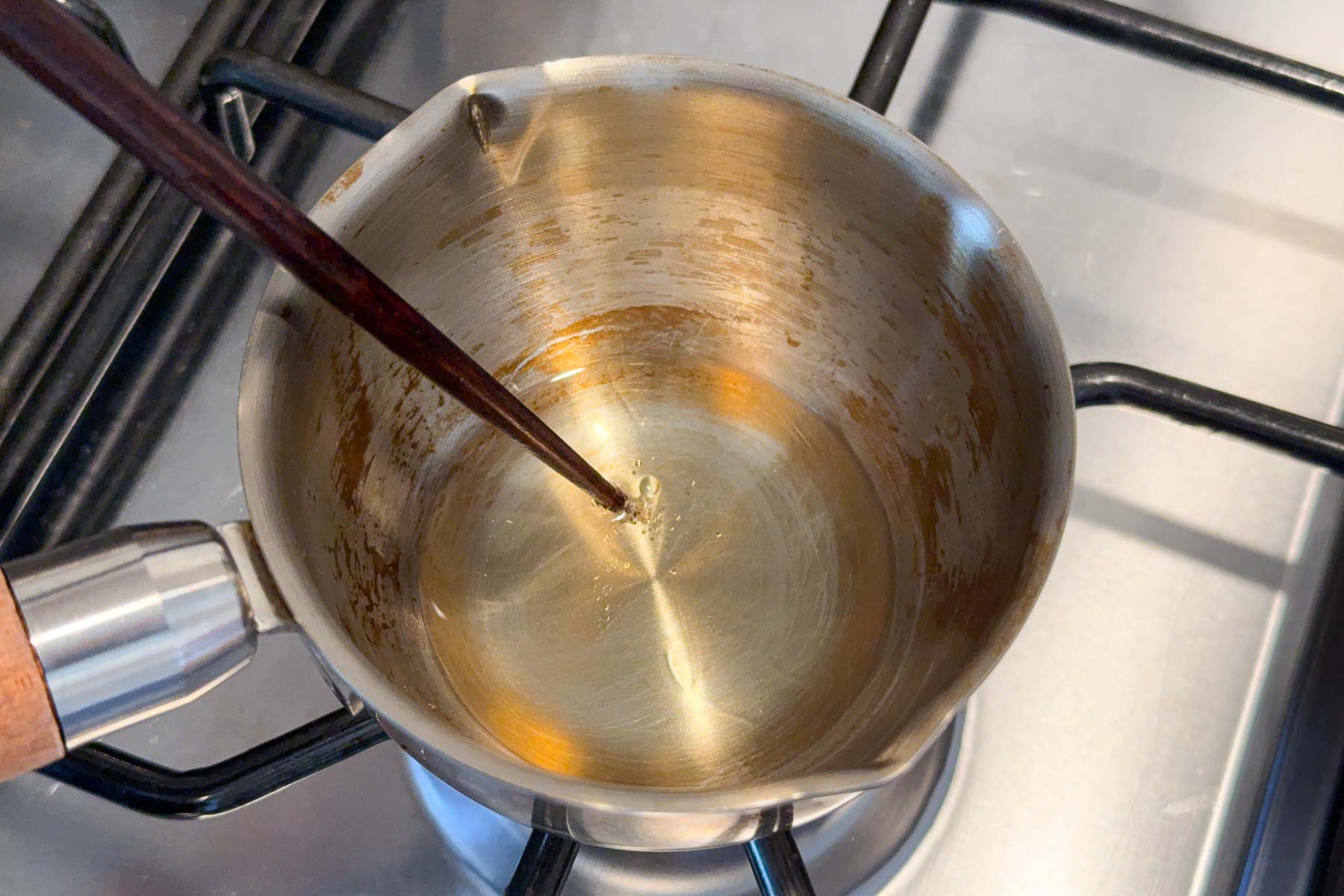 Oil being heated in a small sauce pot on a stove and the tip of a wooden chopstick in the oil, with little bubbles forming around the tip.