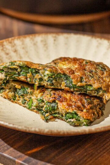 Two slices of golden-brown Chinese Omelette with Basil on a plate, with a skillet in the background.