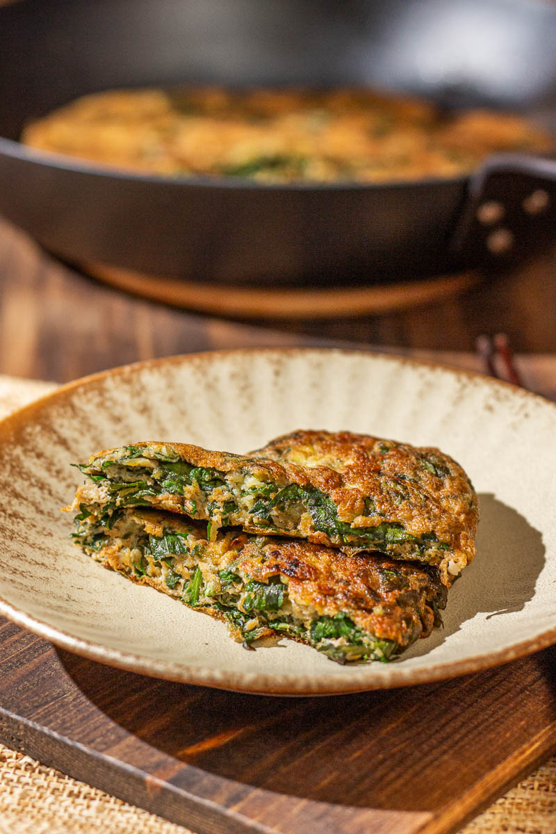 Two slices of golden-brown Chinese Omelette with Basil on a plate, with a skillet in the background.