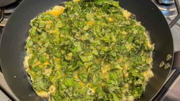 Basil omelette mixture being cooked in a frying pan.