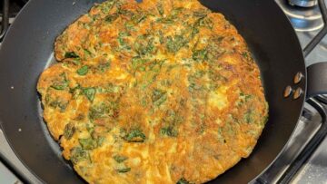 A golden-brown basil omelette in a frying pan on a stove.