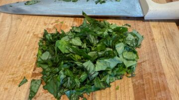 Chopped basil leaves on a wooden cutting board with a knife nearby.