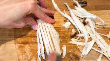 Shredding half of a king oyster mushroom using a fork on a wooden cutting board.
