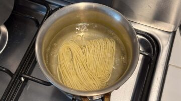 A pot of noodles boils in water on a stovetop, soon to be transformed into delicious cold sesame noodles.