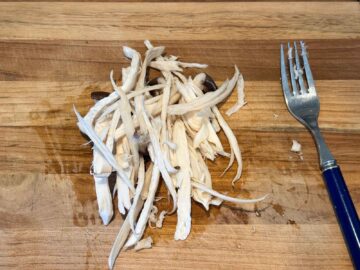 Shredded king oyster mushrooms on a wooden cutting board next to a fork.