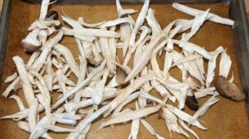 Shredded white mushrooms are spread on a baking sheet lined with a silicone mat, perfect as a topping or side for dishes like cold sesame noodles.