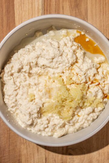 A bowl with mashed silken tofu, pressed garlic, and sesame oil on a wooden surface.