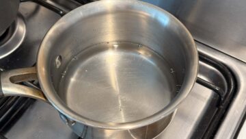 A stainless steel pot with water inside sits on a gas stove, ready to be heated.