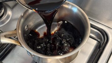 Soy sauce being poured into a stainless pot with water inside on a stove.