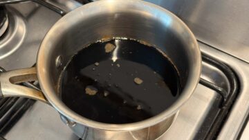 A stainless steel pot with soy sauce and water, simmering on a stove.