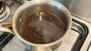 A small stainless pot with thick and sweet soy sauce on a stove, steam rising from the surface.