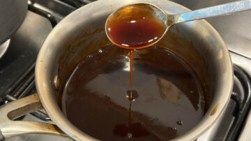 A spoon drizzles thick and sweet sauce over a small pot of the same sauce on a stove.