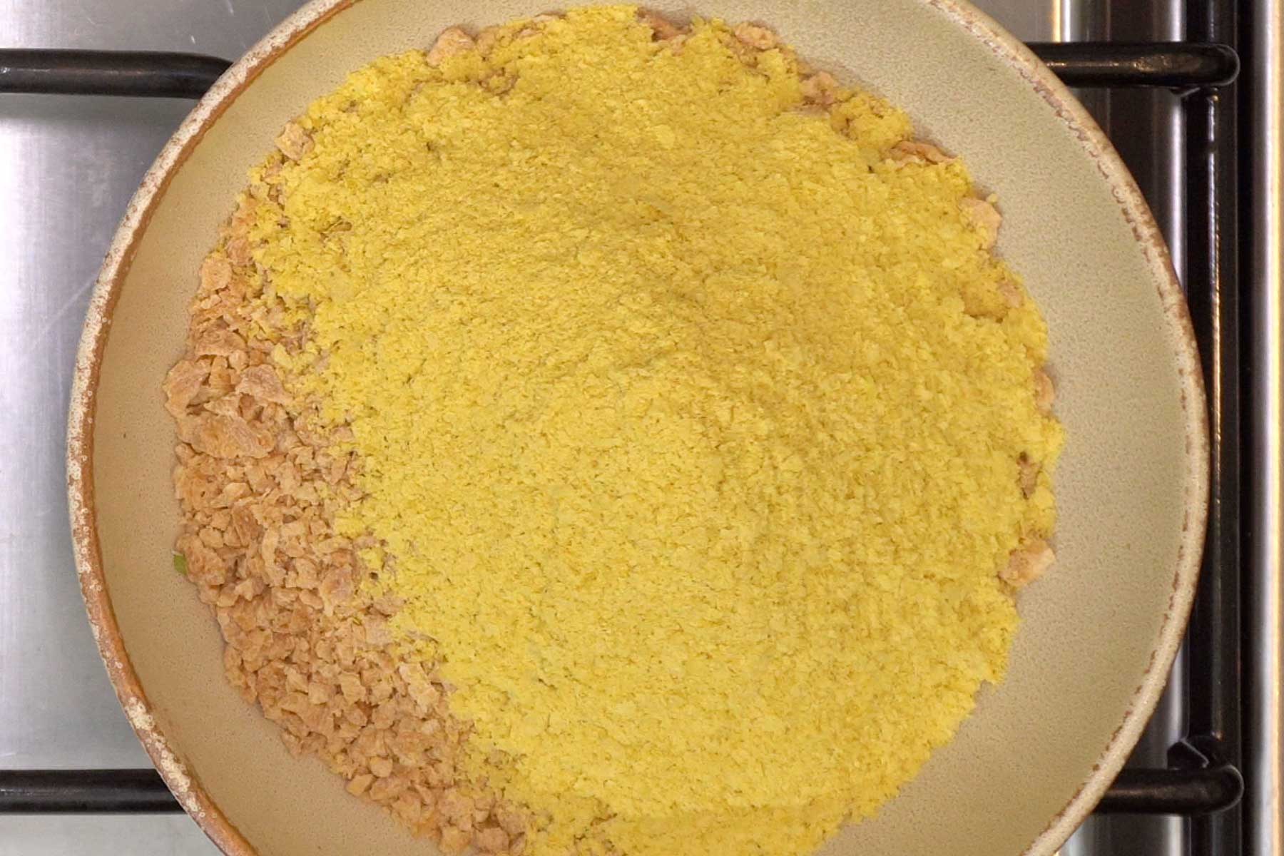 A bowl of light brown Textured Vegetable Protein (TVP) covered in yellow nutritional yeast sits on a stove.