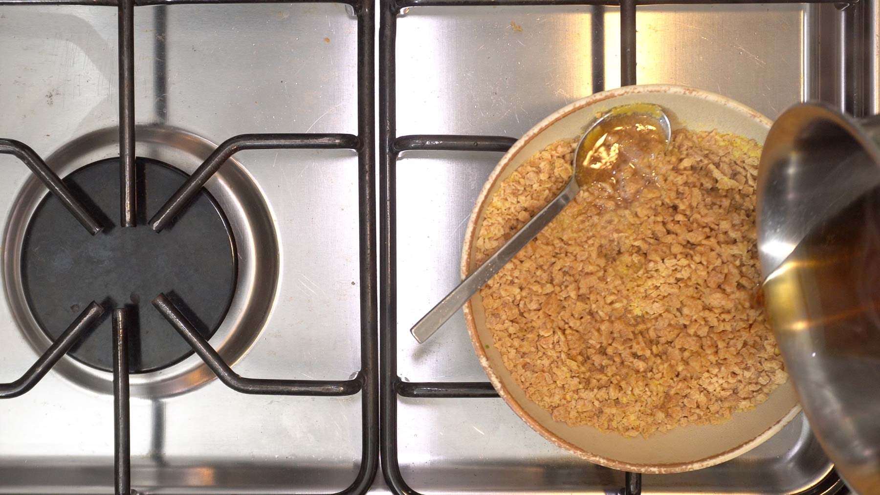 Bowl of Textured Vegetable Protein (TVP) and nutritional yeast on a stovetop, with marinating liquid being poured in from a metal pot.