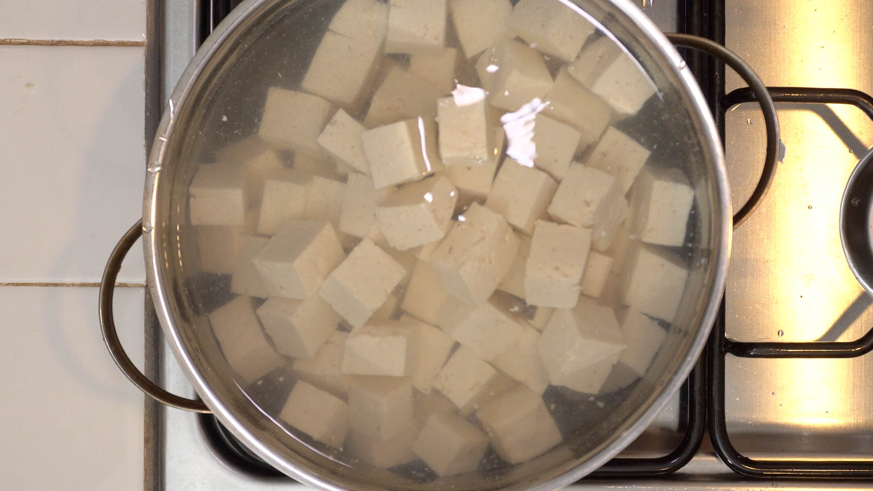 A pot of tofu cubes submerged in water on a stove, viewed from above.