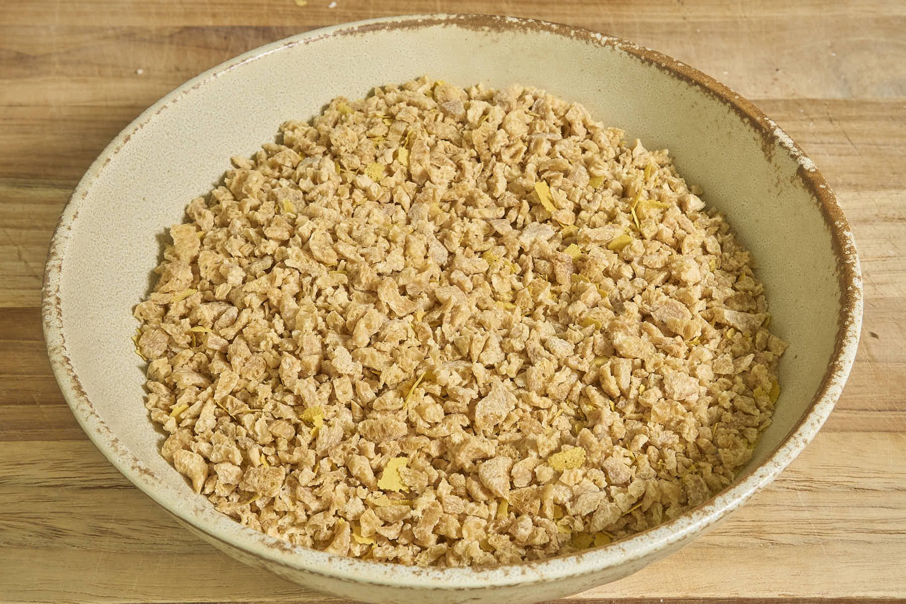 A bowl of dry TVP and nutritional yeast, mixed, on a wooden surface.