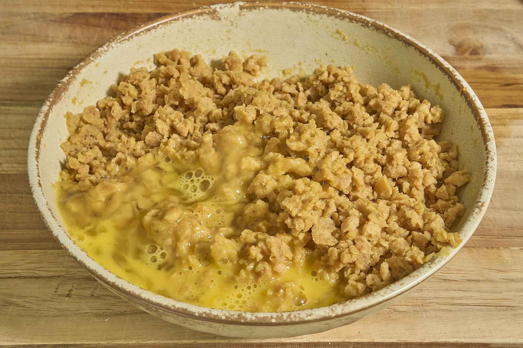 A bowl of marinated TVP and beaten egg mixture on a wooden surface.